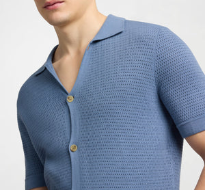 A person wearing the Onia Drop Needle Button Up—a light blue, short-sleeve cotton shirt with textured fabric and two visible buttons—shown from shoulders to mid-torso.