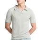 A person wears the Onia Boucle Knit Johnny Polo in light gray, featuring a V-neck, textured boucle yarn fabric, and a relaxed silhouette, while standing with arms behind their back.