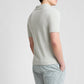 A person stands facing away, wearing the Boucle Knit Johnny Polo by Onia—a light-toned, relaxed fit top—paired with striped shorts, set against a plain background.