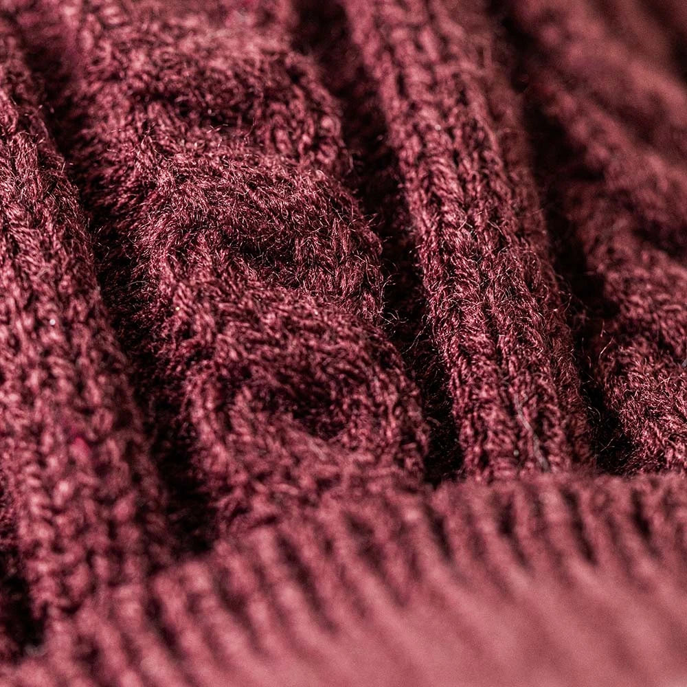 Close-up of a burgundy knitted fabric with a raised cable knit pattern, like the Munro Scottie Dog Winter Jumper Outfit from Jellycat, showing its detailed texture and stitching.