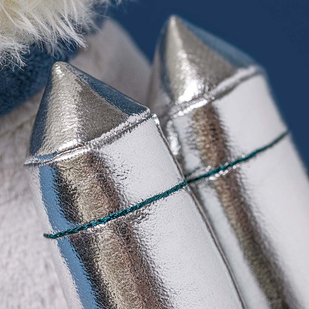 Close-up of two Munro Scottie Dog Space Outfit accessories by Jellycat, featuring metallic silver rocket shapes with textured surfaces, set side by side against a blurred blue and white background for a synthpop feel.