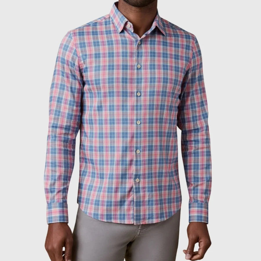A man wearing the Faherty Movement Monterey Shirt—a long-sleeve, button-up featuring a pink, blue, and white plaid pattern—paired with light gray pants. This lightweight and comfortable shirt is wrinkle-resistant, making it perfect for all-day wear.