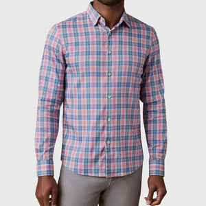 A man wearing the Faherty Movement Monterey Shirt—a long-sleeve, button-up featuring a pink, blue, and white plaid pattern—paired with light gray pants. This lightweight and comfortable shirt is wrinkle-resistant, making it perfect for all-day wear.