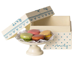 The Maileg Macarons et Chocolat Chaud features five hand-painted macarons held on a white tray, which is positioned beside an open, white keepsake box adorned with blue patterns and the text "Maileg.