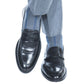 A person wearing gray dress pants, Dapper Classics Steel Gray with Indigo Blue Vertical Stripe Cotton Socks, and black leather loafers with legs crossed at the ankles.