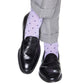 A person wearing black loafers and light gray trousers enjoys the comfort of Dapper Classics Dot Mid Calf Socks, which feature lavender fabric with dark polka dots. These socks from Dapper Classics offer a luxurious feel thanks to their high-quality mercerized cotton, combining style with durability.