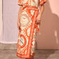 A woman wearing the Maeve Top by Hunter Bell NYC, featuring short sleeves, an orange and cream pattern, a boxy silhouette, and wrap detail, stands on a concrete floor against a neutral background.
