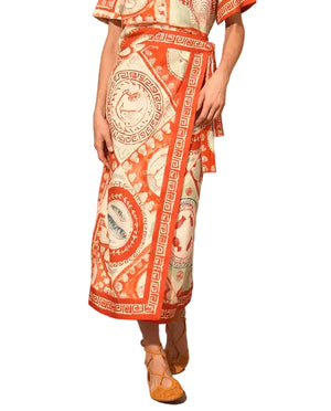 Person wearing an orange and white patterned Paloma Wrap Shirt by Hunter Bell NYC, featuring circular and geometric designs with a waist tie, styled with brown woven shoes.