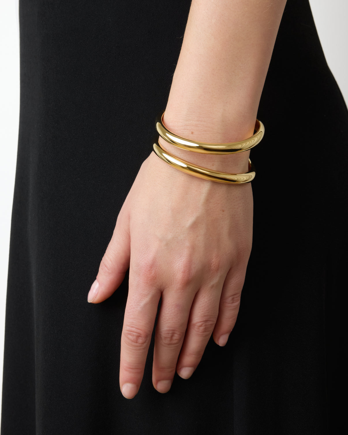 A close-up of a hand wearing three Lie Studio Maggie Bracelets highlights their versatile style, beautifully paired with a black dress.