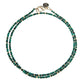 The Jane Win Double Wrap Beaded Necklace features two strands of small, faceted green and gold beads with a gold clasp, artfully arranged in a circular shape on a white background.
