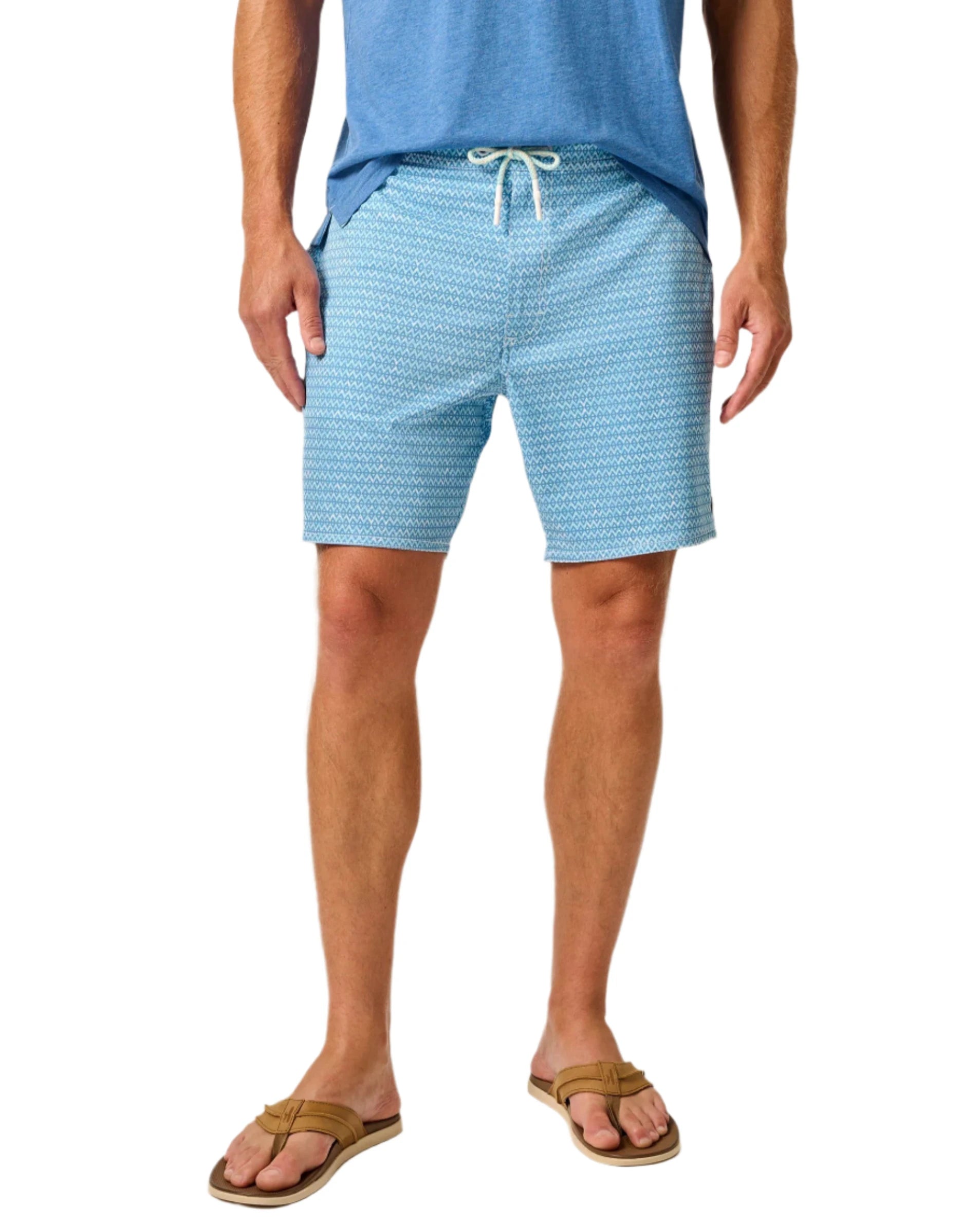 A person wearing a blue Johnnie-O t-shirt and Johnnie-O Malta Swim Trunks, paired with brown sandals.