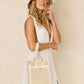 A woman in a sleeveless white dress stands against a plain light background, wearing the Lorna Murray Manhattan Hat and holding a matching beige scalloped tote bag.