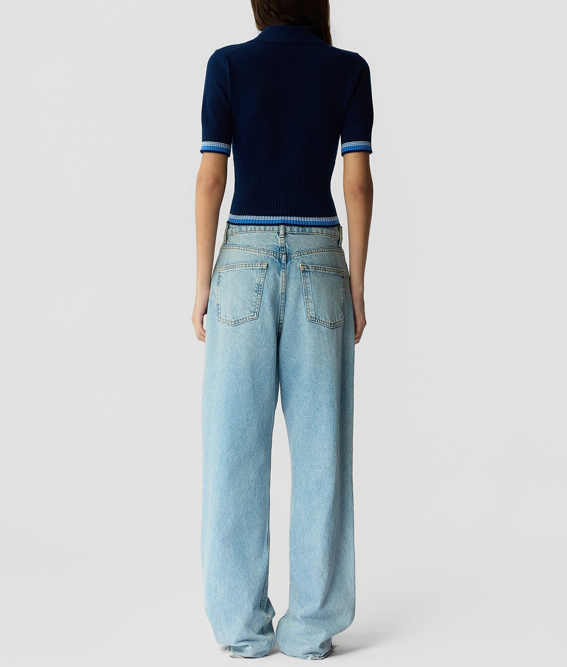 A person faces away, wearing the Marcella Polo by Guest in Residence with loose-fitting light blue jeans against a plain light background.