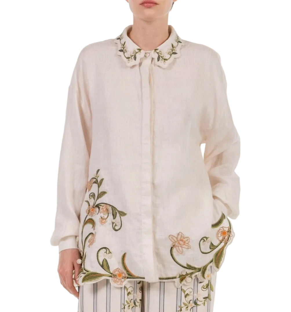 A person wearing the cream floral Cecilia Shirt with embroidered collar and hem by Agua By Agua Bendita, paired with striped pants.