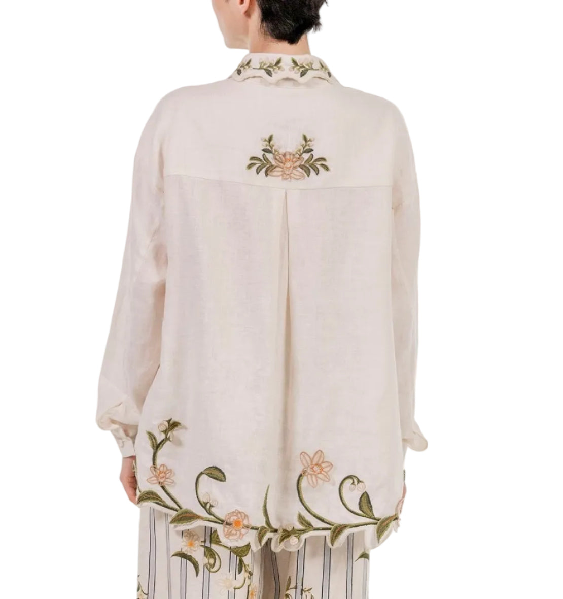 A person, facing away from the camera, wears the Cecilia Shirt by Agua By Agua Bendita with floral embroidery on the back, collar, and hem, paired with matching striped trousers.
