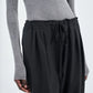 A person wears Maria McManus Barrel Leg Drawstring Trouser, a high-waisted pant crafted from soft Japanese cotton, paired with a ribbed grey long-sleeve top and shown from shoulders to knees.