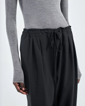 A person wears Maria McManus Barrel Leg Drawstring Trouser, a high-waisted pant crafted from soft Japanese cotton, paired with a ribbed grey long-sleeve top and shown from shoulders to knees.