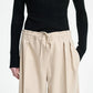 A person wears a black ribbed long-sleeve top paired with the Maria McManus Drawstring Trouser—a high-waisted beige wool-cashmere flannel pant with pleats and drawstring waist—styled for elevated loungewear; shown from shoulders to knees.