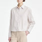 A person wearing a light-colored Maria McManus Button Sleeve Crop Shirt paired with beige trousers stands against a plain background, showcasing a refined cocoon silhouette.