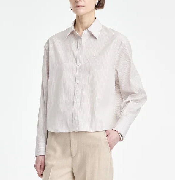 A person wearing a light-colored Maria McManus Button Sleeve Crop Shirt paired with beige trousers stands against a plain background, showcasing a refined cocoon silhouette.