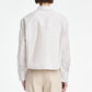 A person is seen from the back against a plain white background, wearing a light-colored Maria McManus Button Sleeve Crop Shirt made from Japanese Supima cotton featuring a cropped silhouette, paired with beige pants.