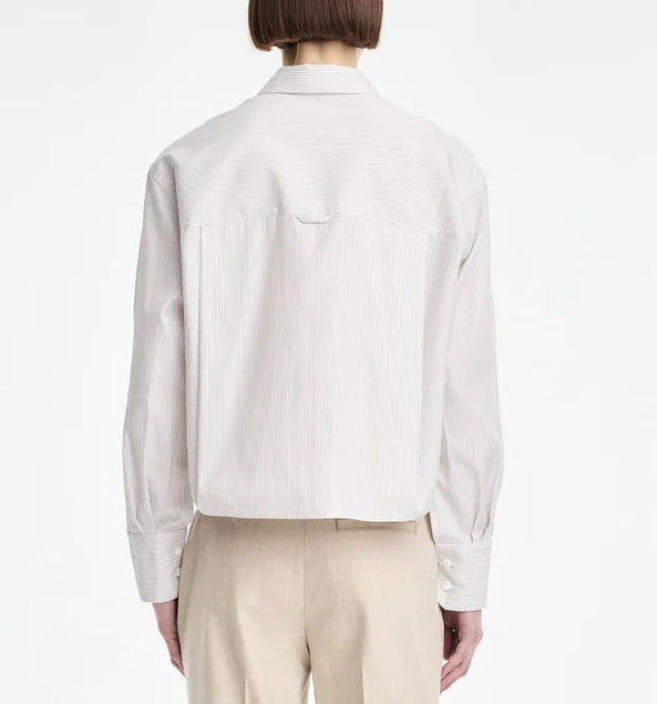 A person is seen from the back against a plain white background, wearing a light-colored Maria McManus Button Sleeve Crop Shirt made from Japanese Supima cotton featuring a cropped silhouette, paired with beige pants.