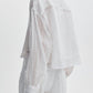 Model shown from the back wearing the Rag & Bone Marin Combo Shirt, a sheer white long-sleeve blouse with a textured pattern and relaxed fit, paired with white pants against a plain background.