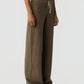 A person is wearing the Marquise Pant by Guest in Residence—loose brown patterned pants with a drawstring waist and straight leg—paired with a white T-shirt and white sneakers, standing against a plain light background.