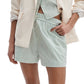 Wearing the Rag & Bone Marvin Stripe Short set—a mint green and white striped shirt with lightweight cotton shorts—styled with a light beige blazer and one hand tucked into the pocket, creating a relaxed silhouette.