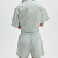 Person facing away from the camera wearing the Rag & Bone Marvin Stripe Short, a light green, short-sleeved, collared romper with vertical stripes, adjustable waist, and elastic waistband.