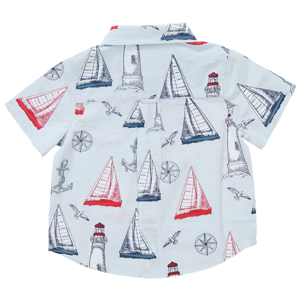 The Boys' Jack Shirt by Pink Chicken is a short-sleeve white shirt with a navy and red nautical print—sailboats, lighthouses, anchors, compasses, and seagulls—ideal for kids who love water adventures.
