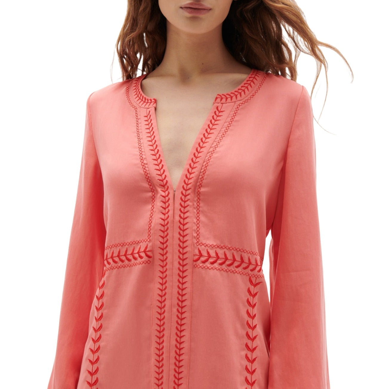 A person wearing the Figue Melissa Dress, a pink dress from the brand Figue, showcases elegant embroidery detailing with long sleeves and a V-neckline.