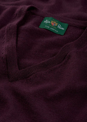 Close-up of a folded dark purple Millbreck V-Neck Merino Wool Sweater with a green label that reads “Alan Paine, Pure Merino.” This classic men’s layering piece by Alan Paine is expertly crafted from premium merino knitwear, offering unparalleled comfort and timeless style.