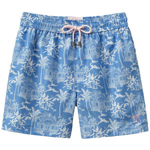 The Pink House Mustique Swim Trunk features a blue design with white tropical house and palm tree print, an elastic waistband, pink drawstring with metal tips, and is made from quick-dry recycled plastic for comfort and sustainability.