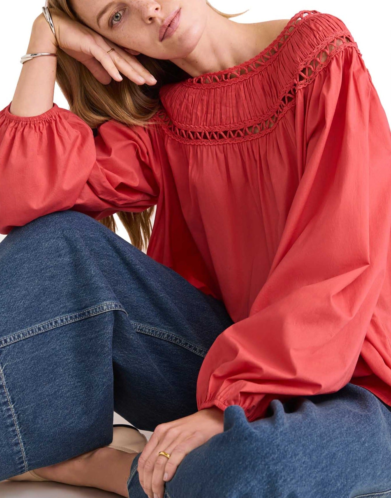 Person wearing a Merlette New York Merlette Ardent Top with intricate handcrafted soutache trim and voluminous sleeves, paired with wide-leg blue jeans, sitting and gazing thoughtfully.