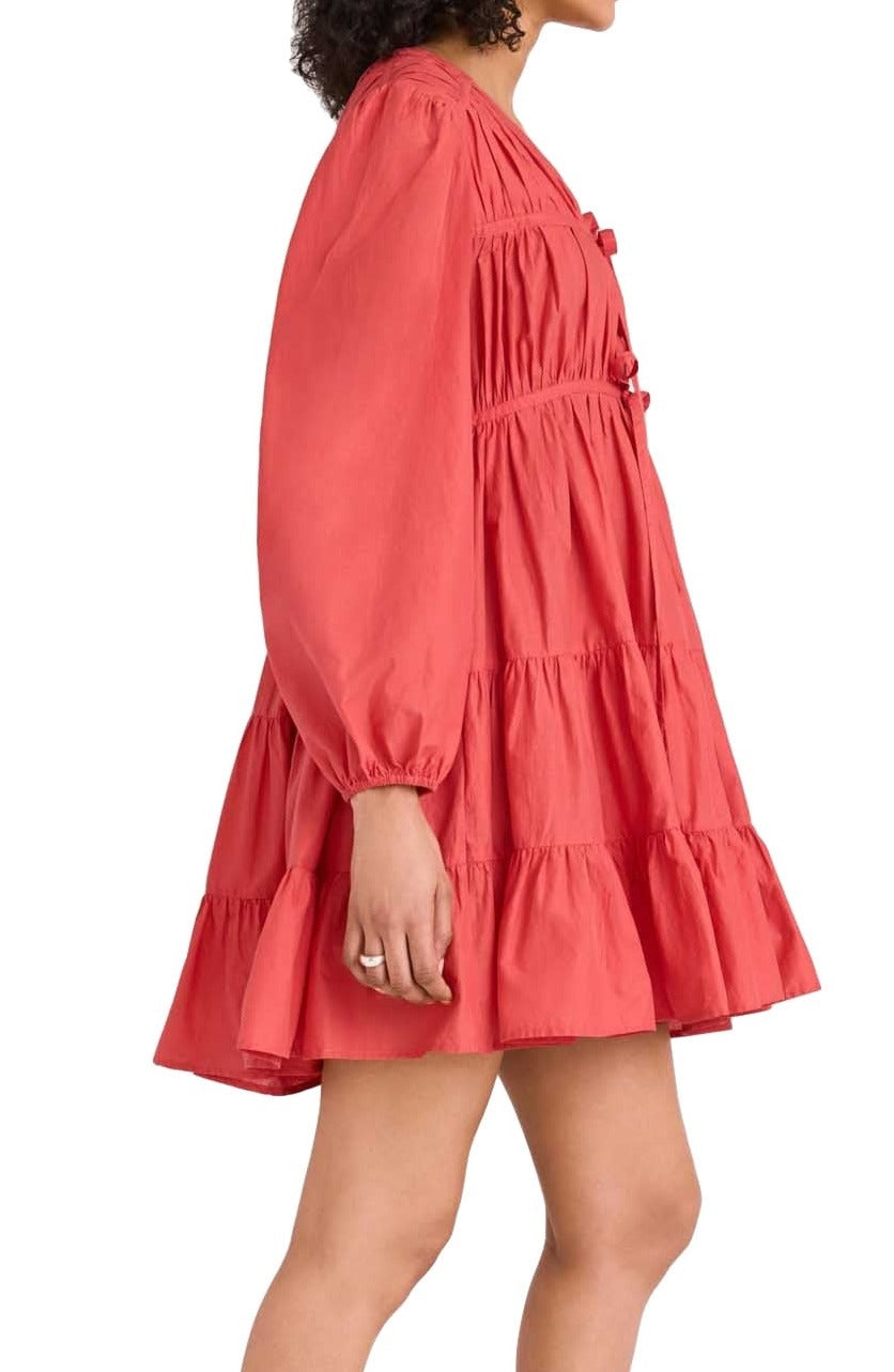 Side view of a woman wearing a Merlette New York Lasse Dress, a coral red long-sleeve mini dress with tiered construction, focusing on the details and flow of the fabric.