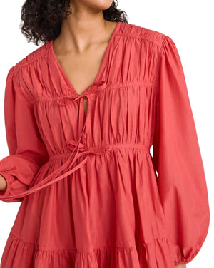 Close-up of a woman wearing a Merlette New York Merlette Lasse Dress, a coral red, long-sleeve mini dress with detailed ruching at the chest.