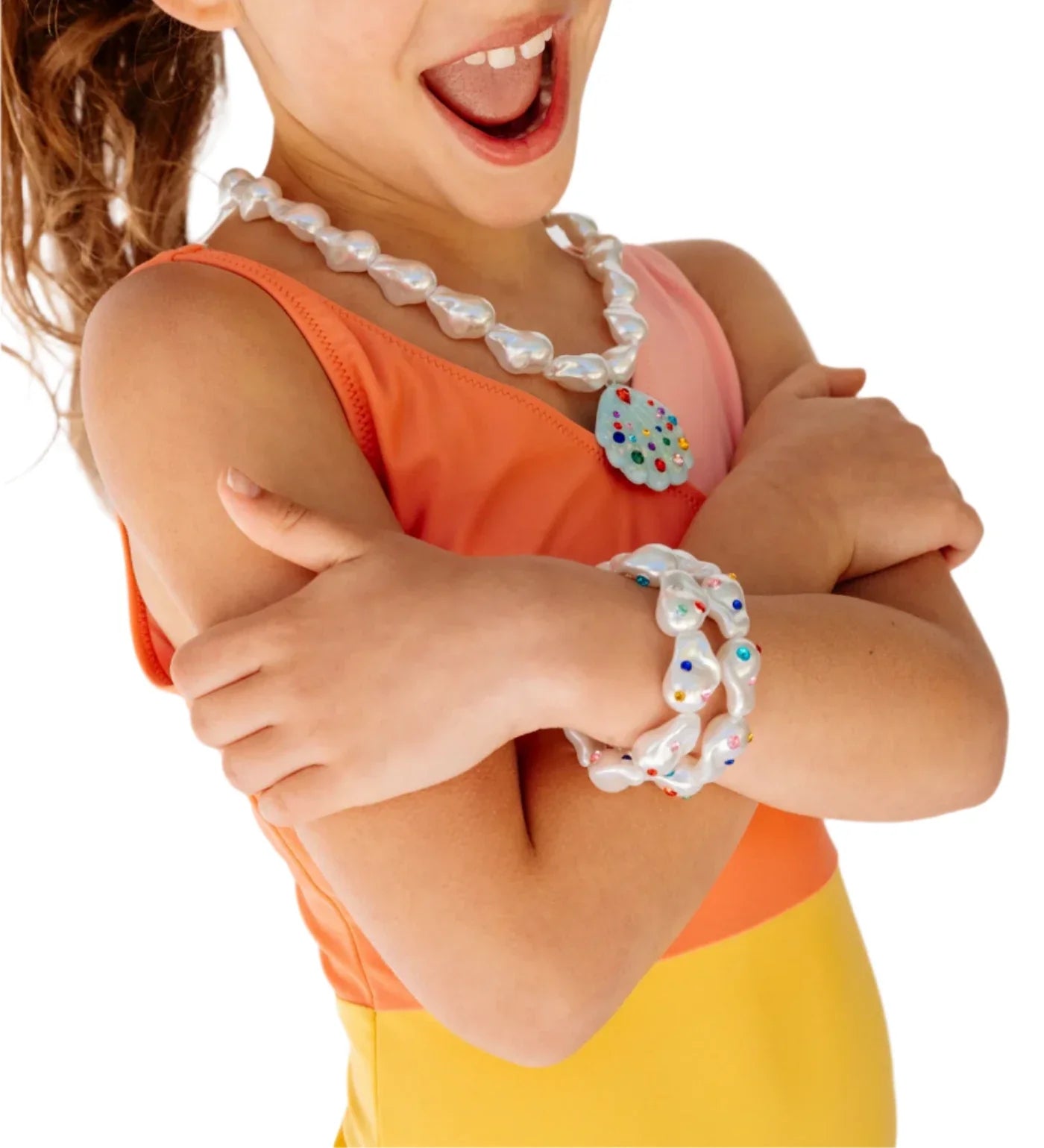 A child in a sleeveless orange and yellow kids' summer set crosses their arms while wearing the Super Smalls Supersmalls Mermaid Pool Party Mega Set, complete with a beaded necklace and bracelet.