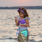 A child in a Great Pretenders Mermaid Dress & Headband delights in ice cream on the beach at sunset.