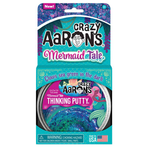 The packaging of Crazy Aaron's Thinking Putty, Mermaid Tale edition, showcases a glittery design. This non-toxic silicone putty glows sea green in the dark, making it ideal for sensory integration. It includes a warning label for choking hazards and is proudly made in the USA by Crazy Aarons.