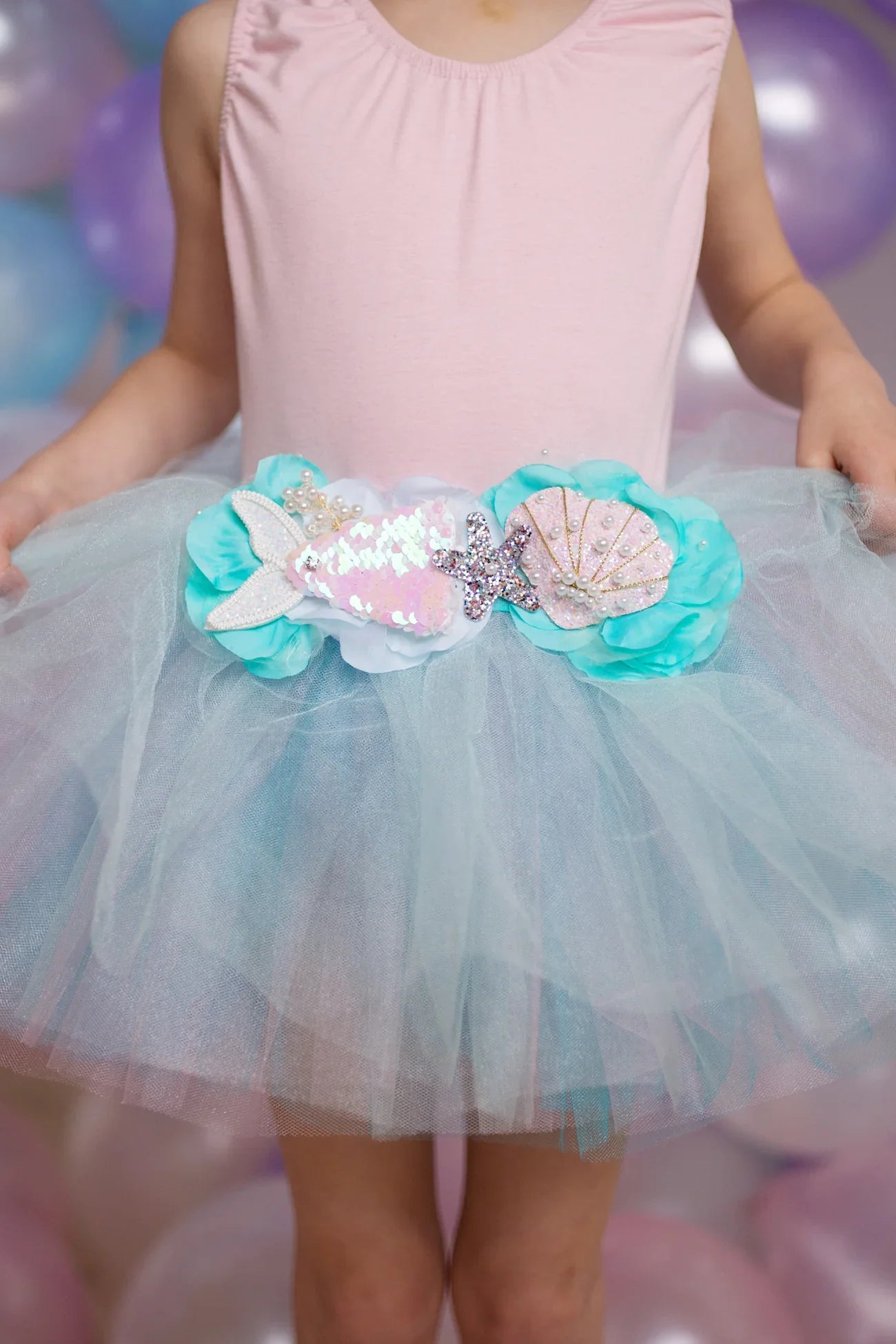 A child was wearing a light pink top and the Great Pretenders Mermalicious Tutu, a light blue tulle skirt from the Great Pretenders brand that features a decorative waistband with mermaid embellishments like sequin fish and shells.