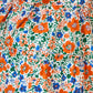 Close-up of the Girls' Merritt Dress by Hunter Bell NYC: floral fabric with red-orange, blue, and green flowers and leaves on white, inspired by the original design and finished with a charming ruffled neckline.