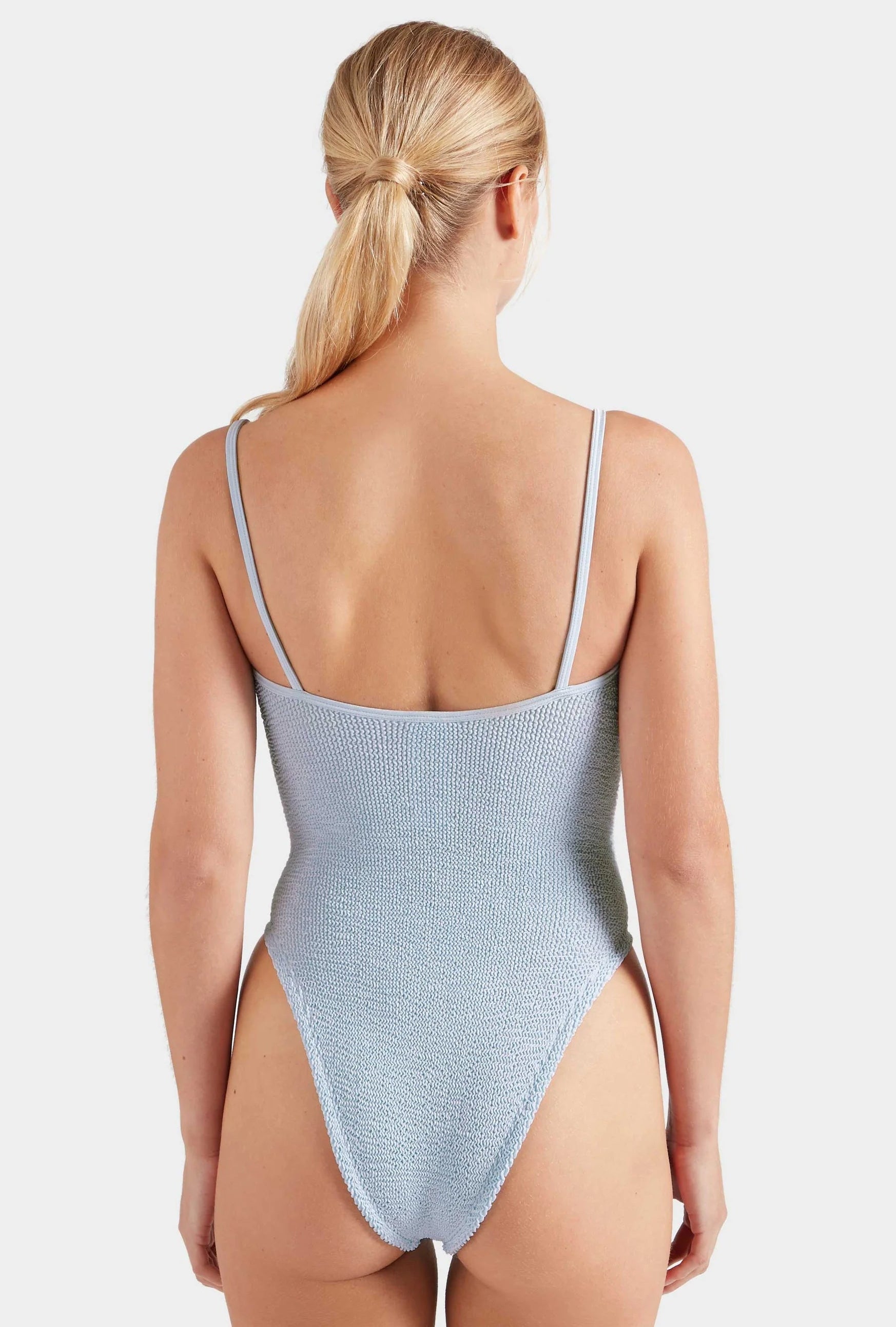 Woman with blonde hair in a ponytail wearing the Hunza G Mia Beaded Swim in light blue crinkle fabric, viewed from the back against a plain white background.