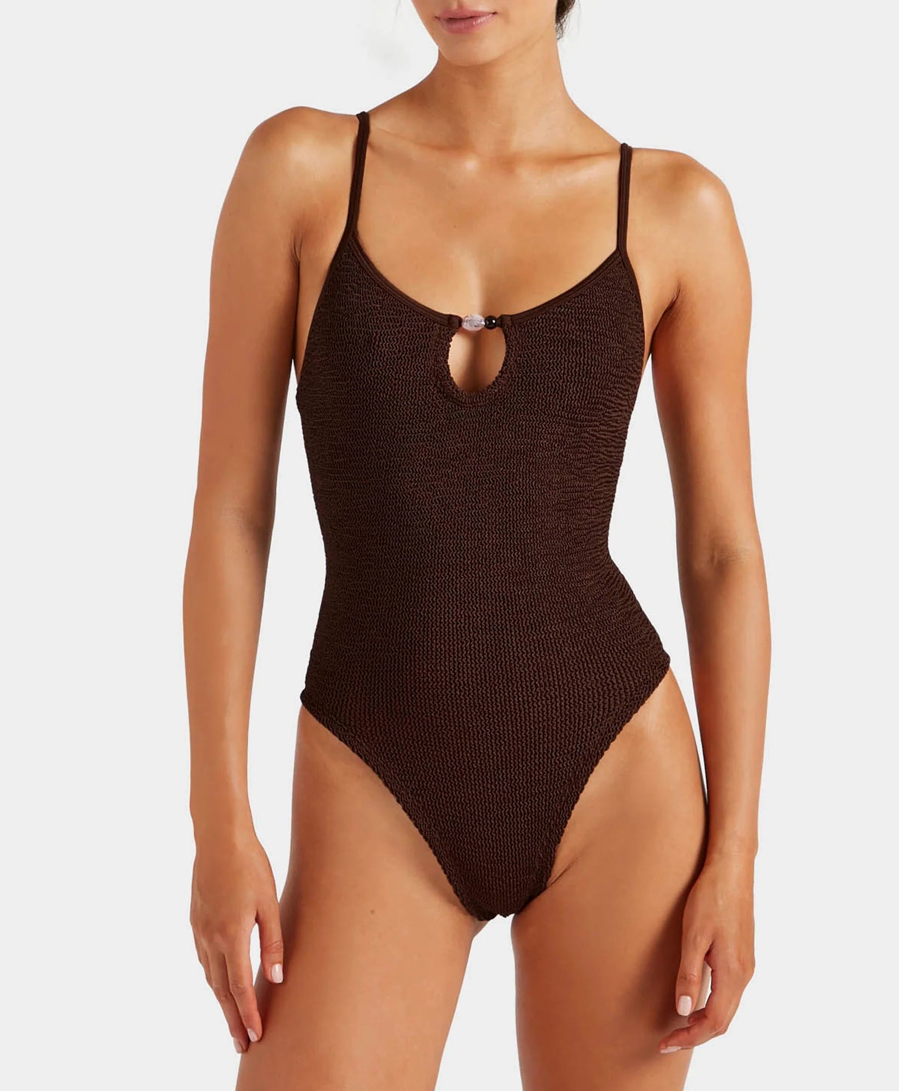 A woman wearing the Hunza G Mia Beaded Swim one-piece in dark brown, featuring thin straps and a small front keyhole cutout.