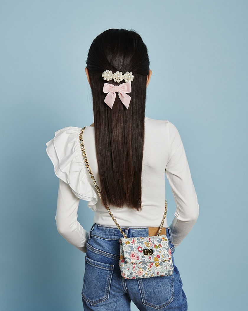 Woman from behind showcasing a floral hair accessory made from Milledeux Small Chain Bag, Liberty Print fabric and a decorative quilted flap bag with metal closure.