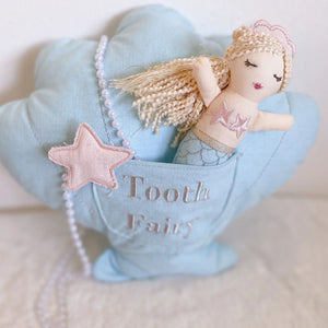 The Mon Ami Mimi Mermaid Tooth Fairy Pillow Doll Set features a plush mermaid doll nestled in a blue shell-shaped pocket, adorned with a star and pearl-like beads, making it ideal for enchanting bedtime rituals.