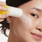 A person applies Supergoop Mineral Sheer Stick SPF 30 to their cheek, holding the yellow-capped applicator close to their face.