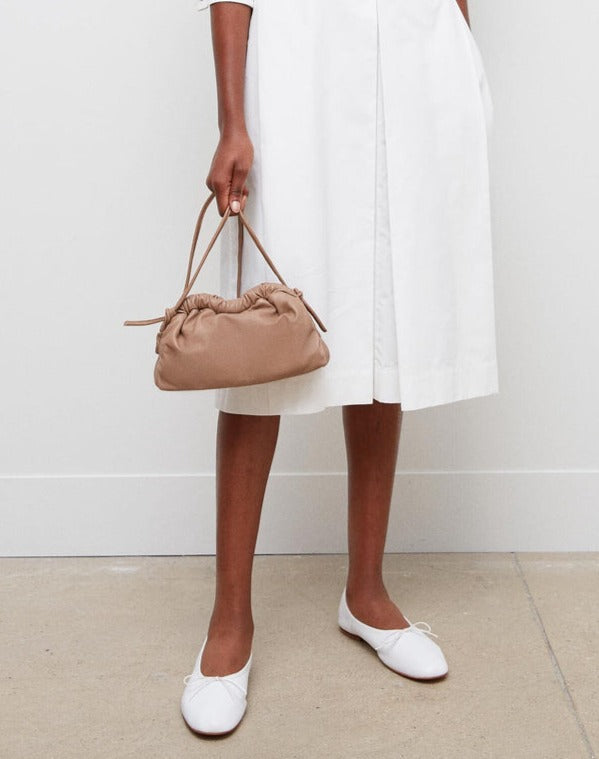 Person wearing a white dress and white shoes holding a Mansur Gavriel Mini Cloud Clutch with a multi-function strap.