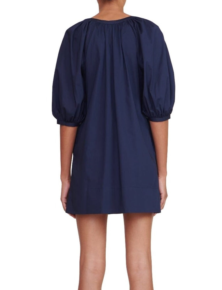 A woman in a navy puff sleeve Staud Mini Vincent Dress made from cotton poplin fabric.