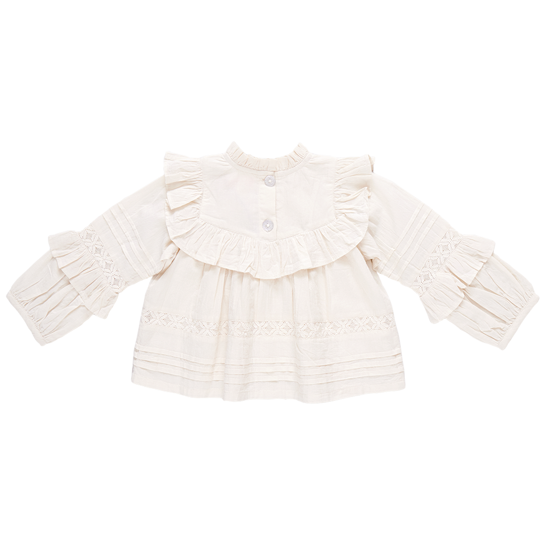 A cream-colored Lace Mira top by Pink Chicken, featuring long sleeves, a ruffled collar, and decorative lace detailing, made from 100% cotton cambric.